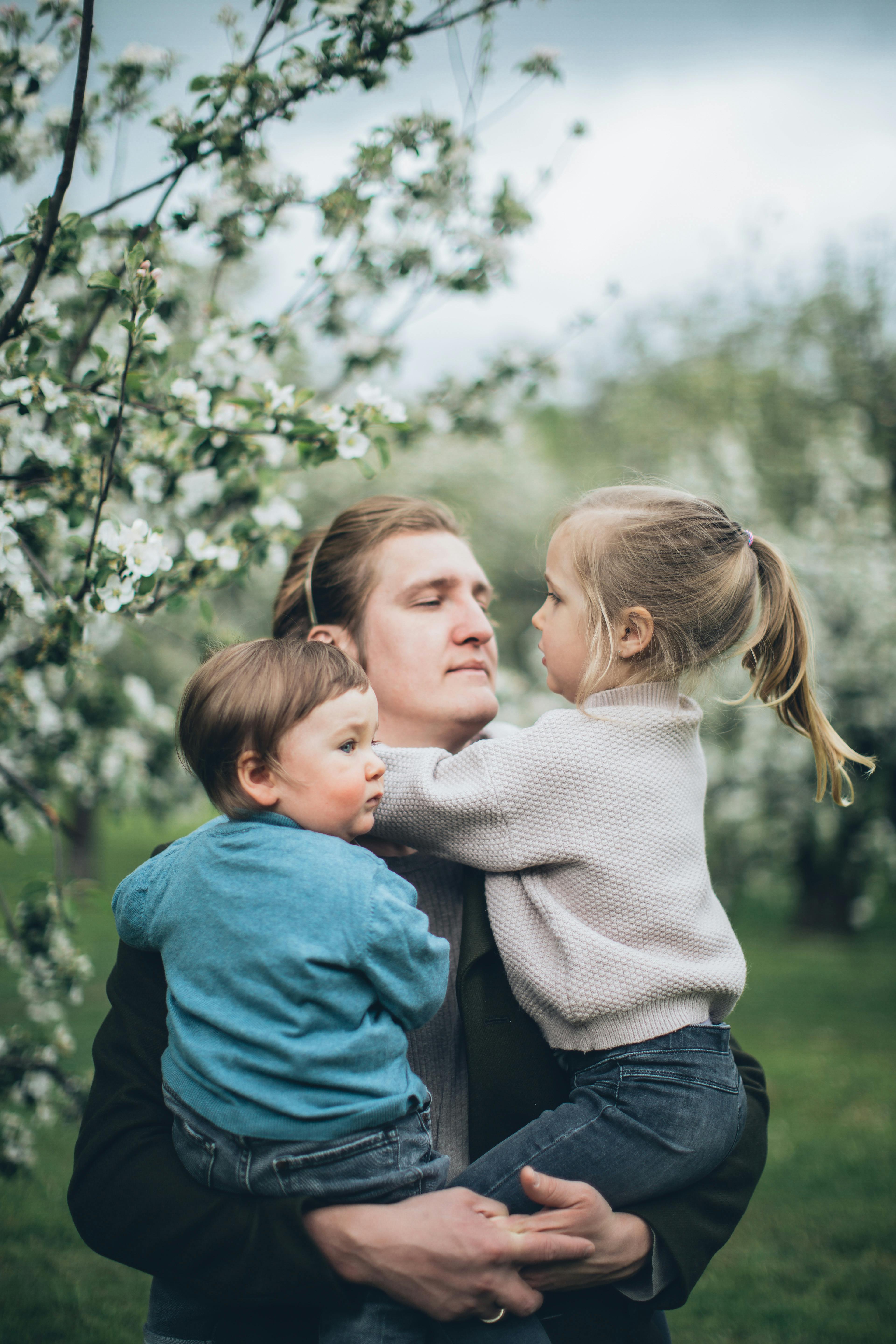 Father holding and playing with children in an orchard