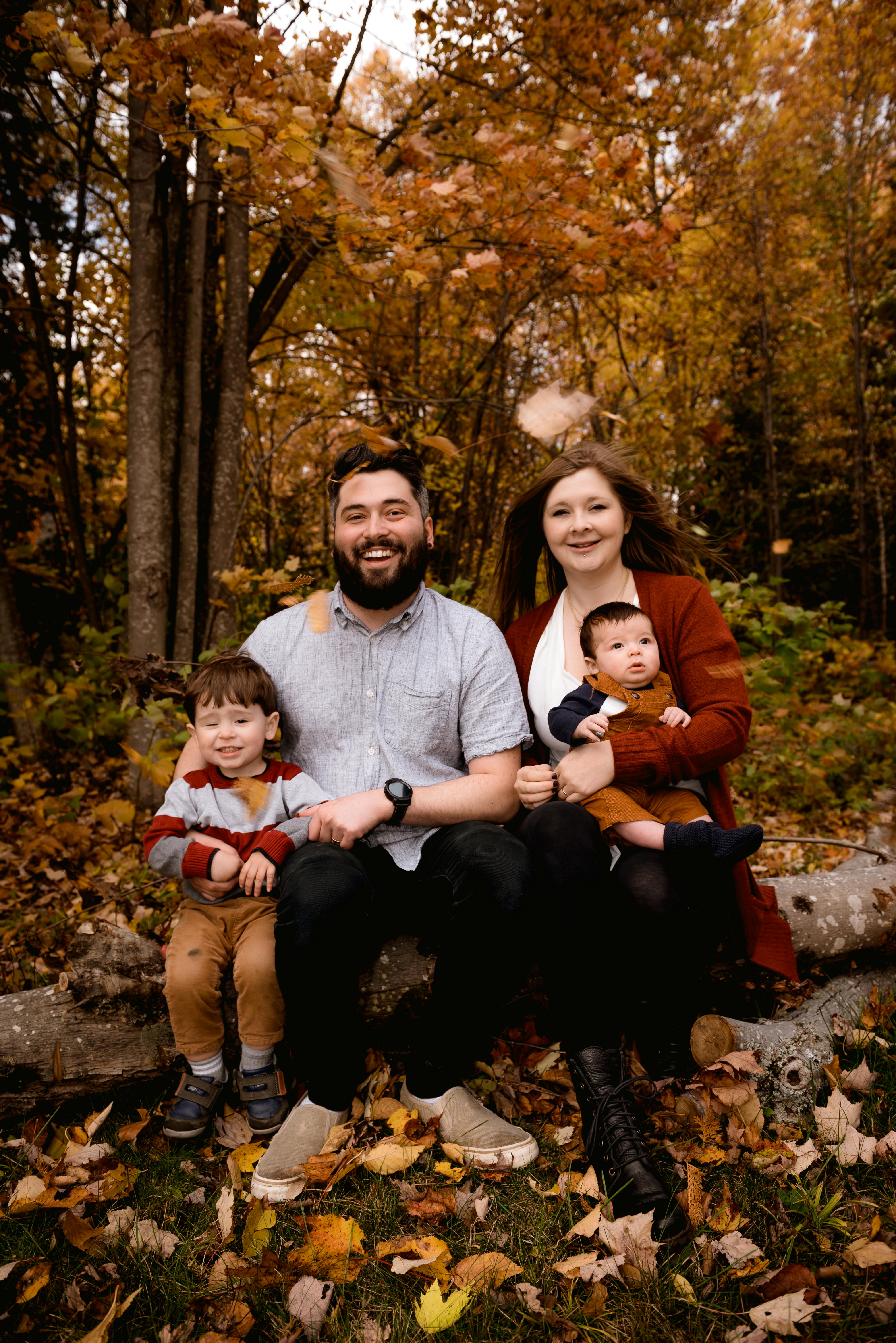 Multigenerational family resting together on a fallen log in a sunlit forest, evoking the road-trips and outdoor leisure that retirees who travel build their schedule around