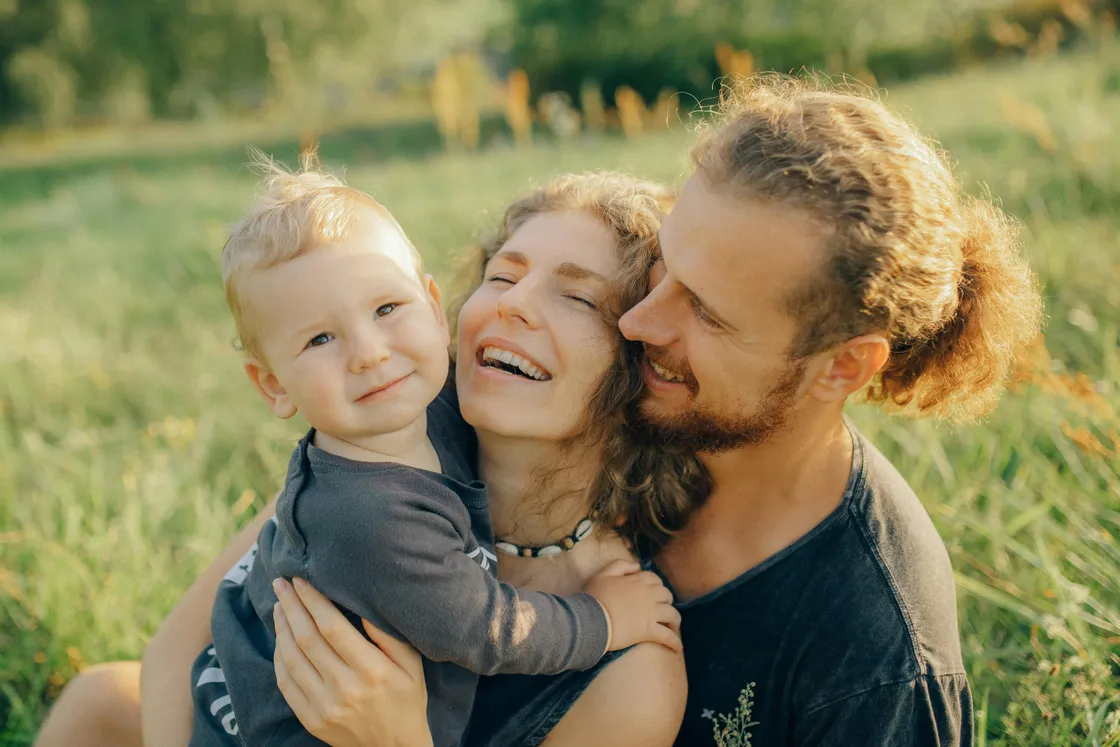 New dad with partner and blond baby in a sunny Florida meadow, representing first-year fatherhood and the need for term life insurance