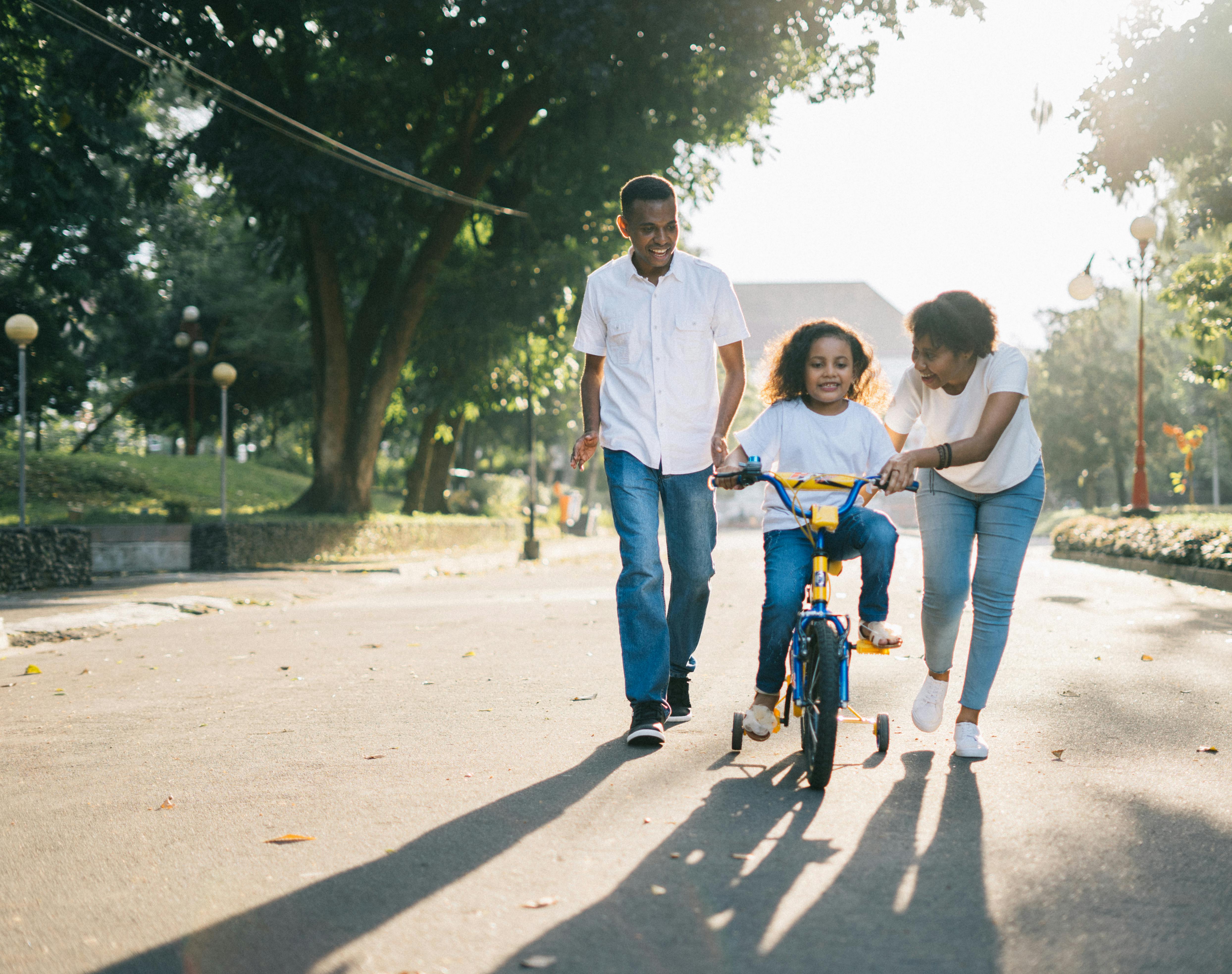 Florida mother and father walking alongside their child as the child learns to ride a bicycle on a sunny day outdoors