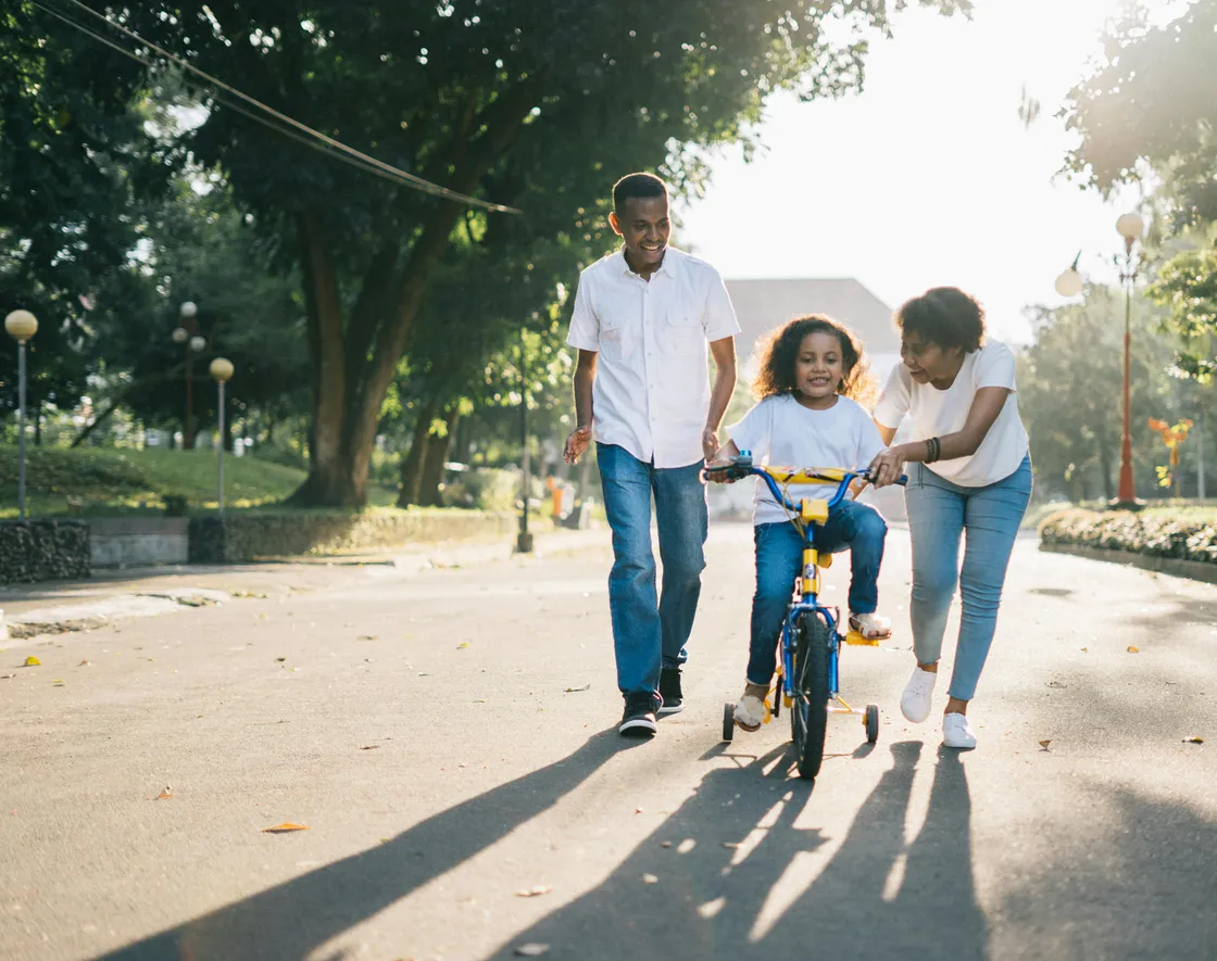 Florida parents walking alongside a child learning to ride a bicycle on a sunny suburban path