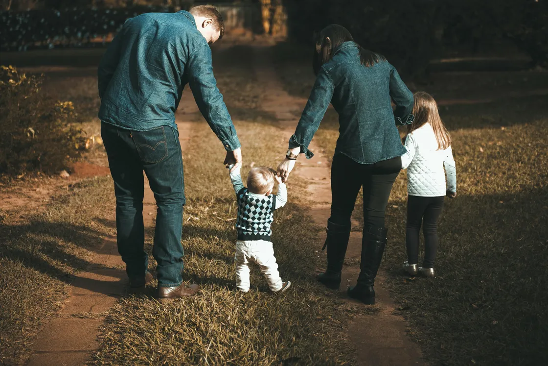 Florida toddler walking between parents on a grass lawn with arms outstretched, capturing the family milestone that signals it's time to review life insurance coverage
